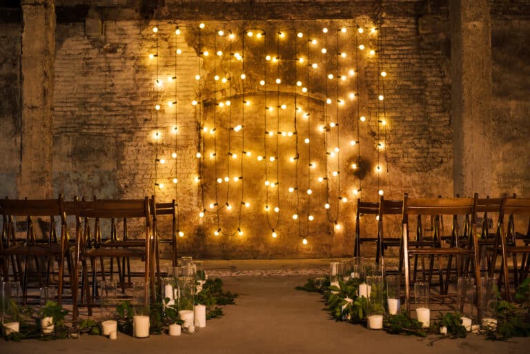 Wedding ceremony decorations in loft grunge surround. Light bulb garland, candles, glass and chairs